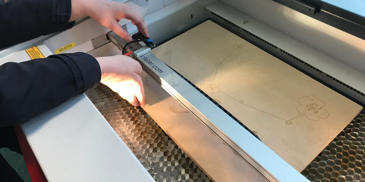 Operator adjusting Trotec Speedy CO₂ laser cutter during floral design engraving on wood