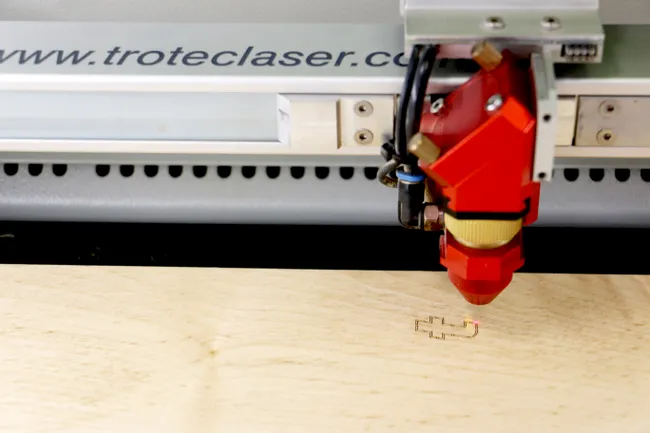 Trotec CO₂ laser cutter engraving a shape on light wood surface
