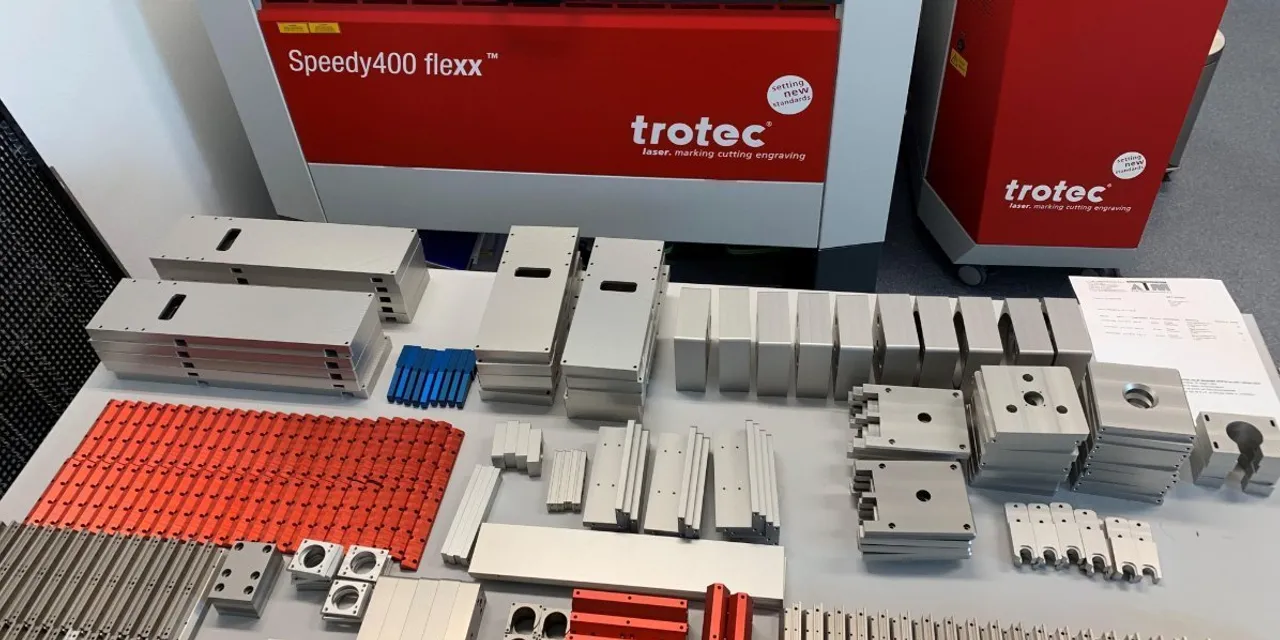 Trotec Speedy400 flexx laser cutter with precision-cut metal parts displayed on table