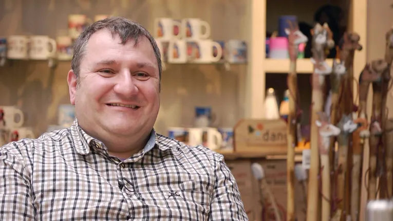Man smiling in store with engraved mugs and laser-cut wood crafts in background
