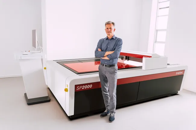 Man standing beside Trotec SP2000 large-format CO₂ laser cutter in modern workspace