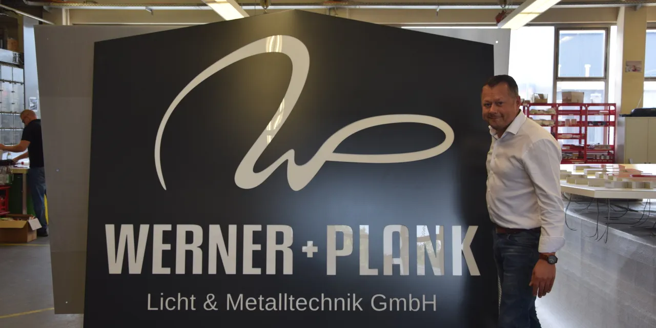 Man standing beside large laser-cut metal sign for WERNER + PLANK Licht & Metalltechnik GmbH