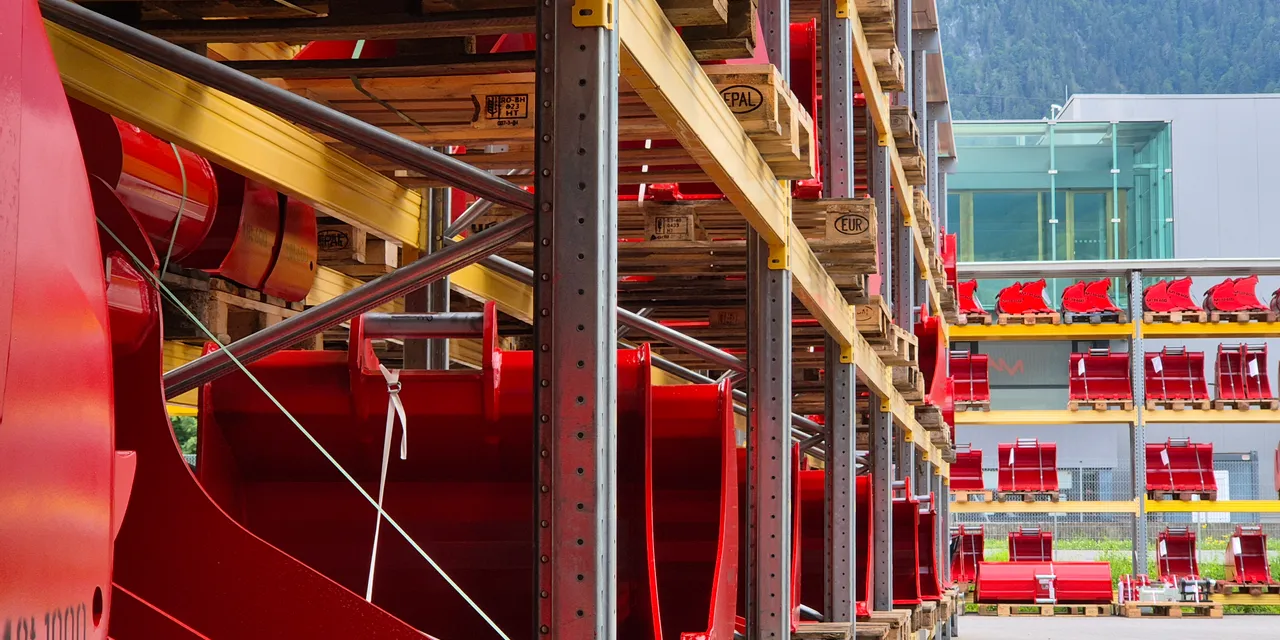 Outdoor storage racks holding red industrial machine parts on wooden pallets near factory