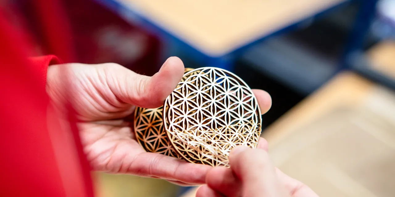 Person holding intricately cut wooden coasters made with Trotec® 快乐幸运8手机澳洲版 CO₂ Laser 今日官方最新168体彩澳洲8结果幸运号码记录查询 cutter