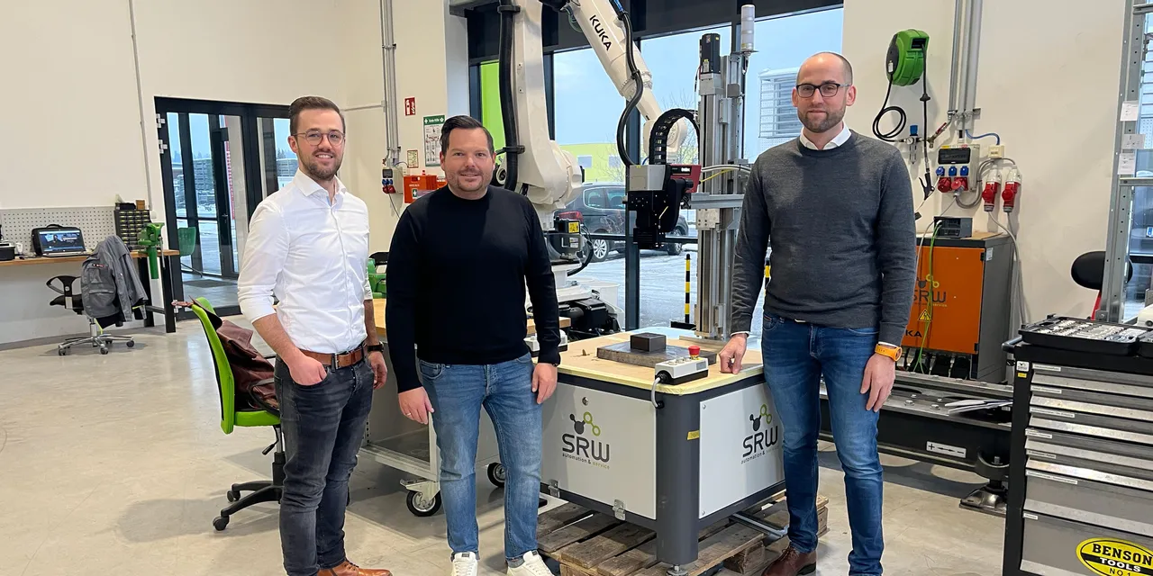 Three men standing in front of industrial SRW robot arm system in modern laser technology workspace