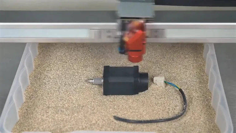 Trotec laser cutter engraving a black plastic part inside a tray filled with sand