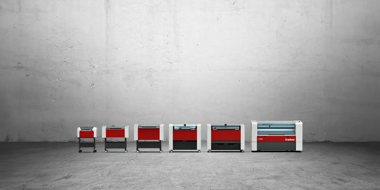 Trotec Speedy series CO₂ laser engravers of various sizes lined up against a concrete wall